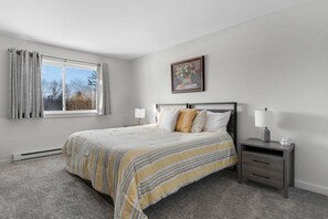 Una camera da letto con un letto, comodini, una finestra con tende, un quadro appeso e un termosifone.