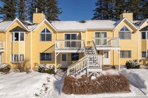 Un edificio giallo a più piani con una scala centrale, balconi e terreno innevato.