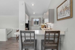 A modern kitchen with a central island, two bar stools, and a painting on the wall. - Bethel Inn Townhouse 524 (Bethel)
