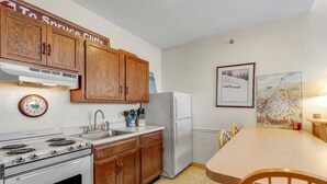 A kitchen with wooden cabinets, a stove, a refrigerator, a sink, and a dining table with chairs.