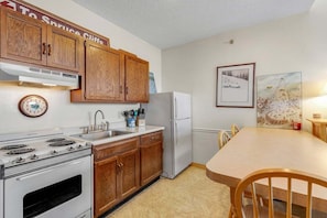 A kitchen with wooden cabinets, a stove, a refrigerator, a sink, and a dining table with chairs.