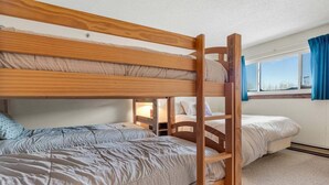 A bunk bed room with a wooden ladder, a window with curtains, and a carpeted floor.