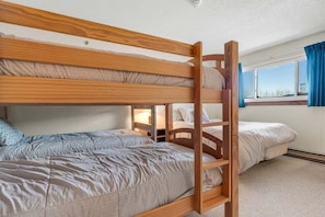 A bunk bed room with a wooden ladder, a window with curtains, and a carpeted floor.