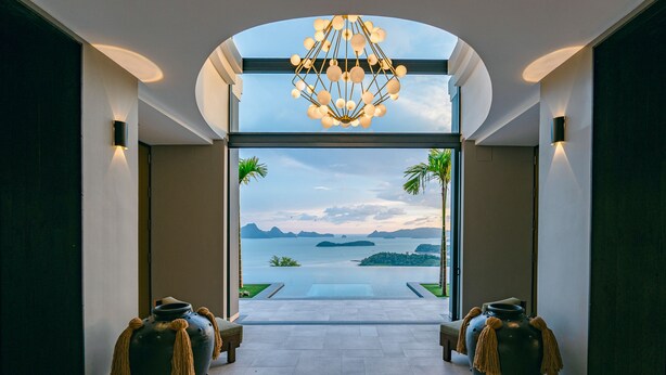A modern interior with a view of a calm sea and islands. There are two large vases with tassels at the entrance.