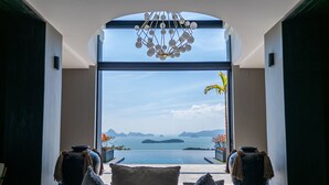 A modern interior with a large window offering a view of a body of water and islands. There are two large vases and a wicker chair with cushions.
