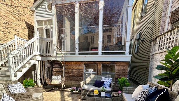 A patio with wicker furniture, a hanging chair, and a staircase leading to an upper level. - Ideal Group Getaway: Prime Location, Parking, Backyard, Sunroom & Pet-Friendly (Chicago)
