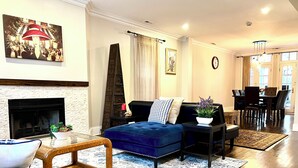 A living room with a fireplace, a blue sofa, a wooden coffee table, and a dining area with a chandelier. - Ideal Group Getaway: Prime Location, Parking, Backyard, Sunroom & Pet-Friendly (Chicago)