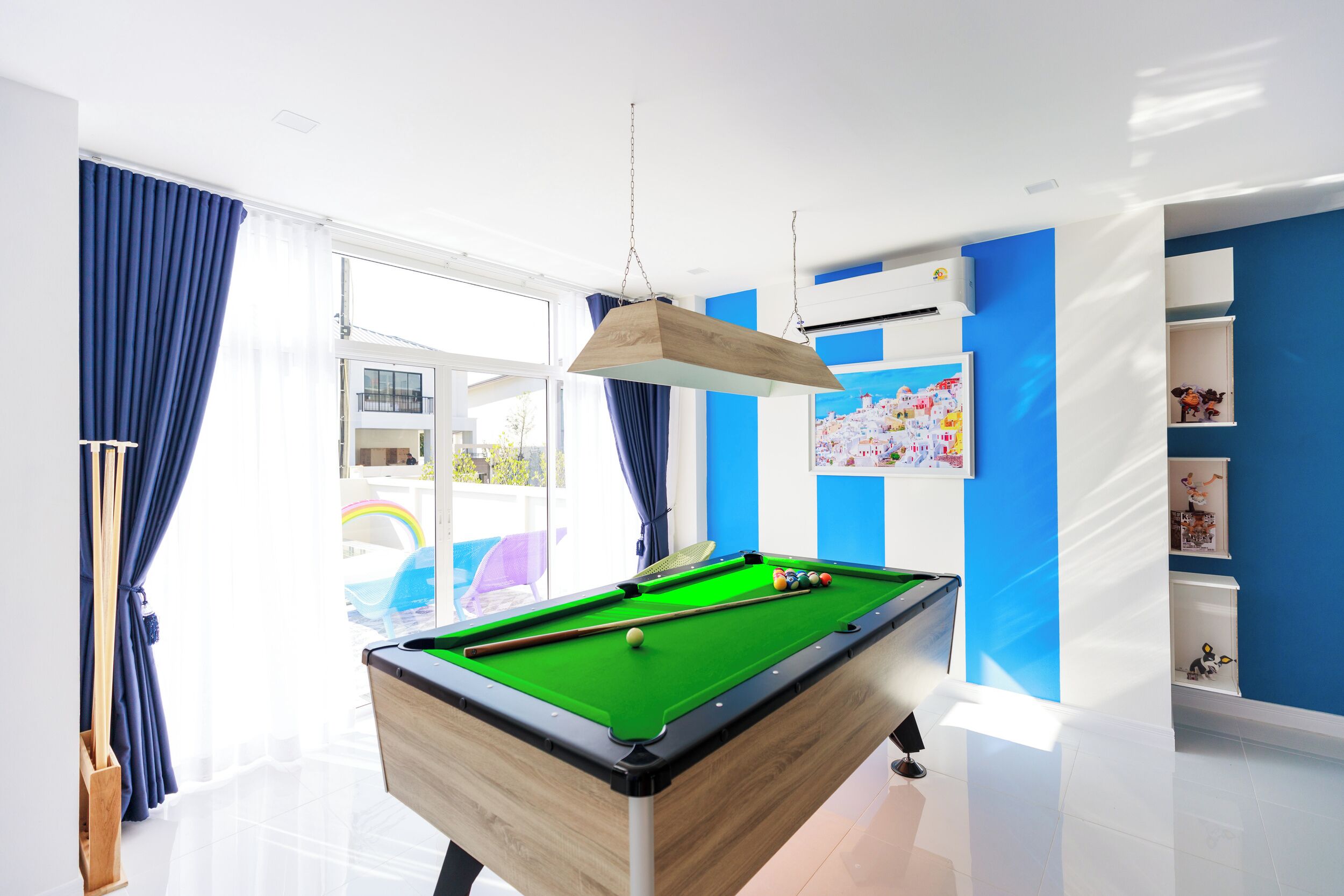 A pool table in a bright room with blue walls and large windows.