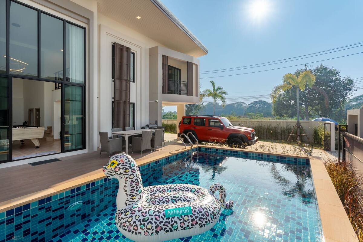 A modern house with a swimming pool, a red SUV, and a pool float shaped like a swan.