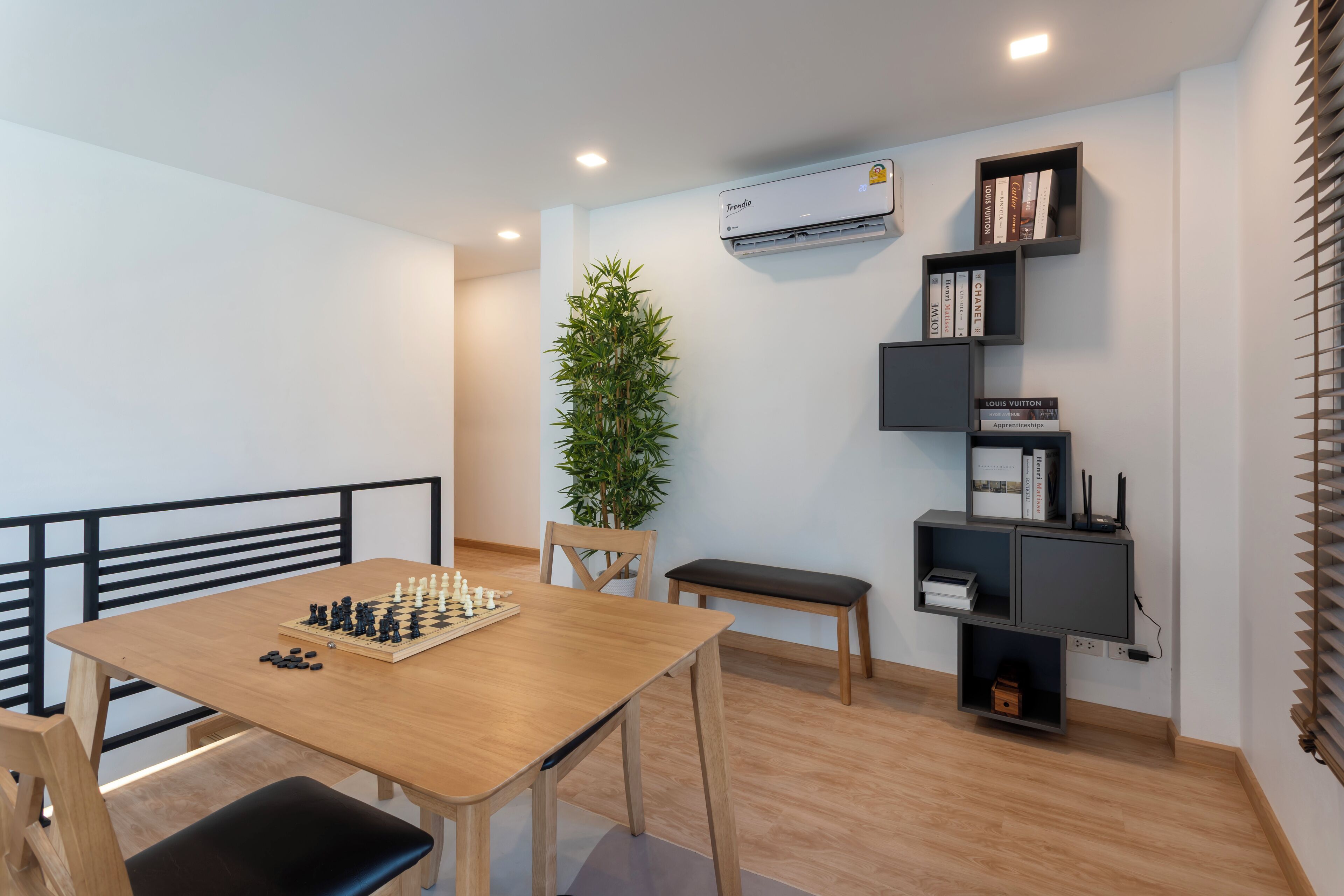 Une chambre moderne avec une table en bois, un jeu d’échecs, une plante en pot et une bibliothèque contenant des livres et un article de la marque Louis Vuitton.
