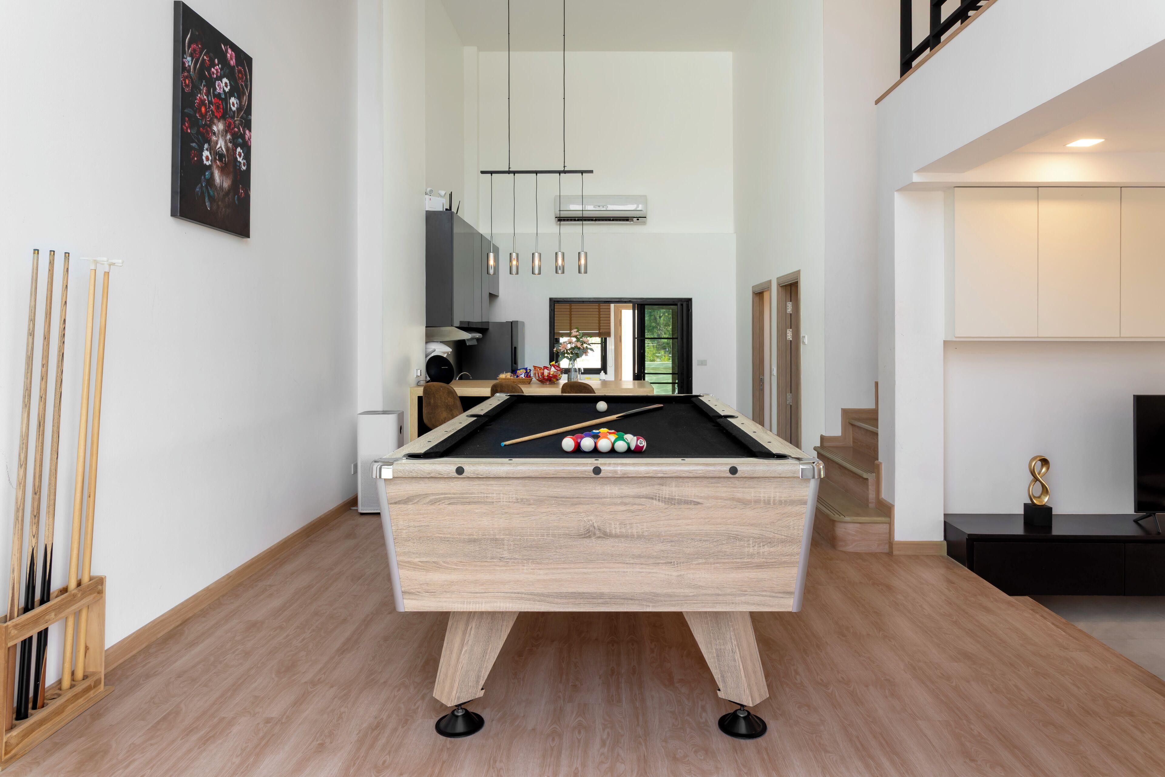 A modern living room with a pool table, a wooden floor, and a staircase leading to an upper level.