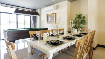 A dining area with a pool table, a dining table set for six with chairs, a vase with branches, and a framed picture on the wall.