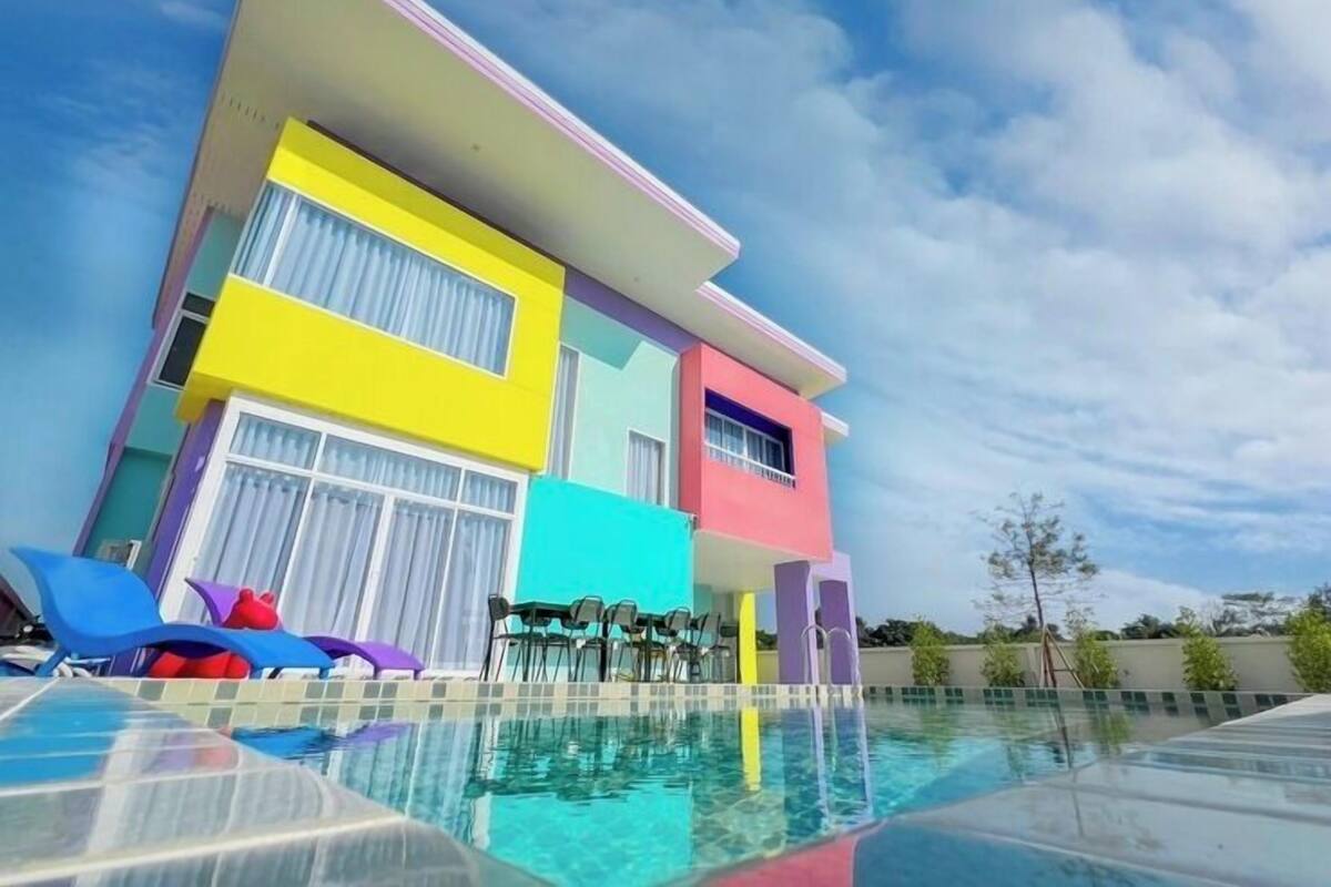A colorful hotel with a swimming pool, featuring a modern architectural design and outdoor seating area.