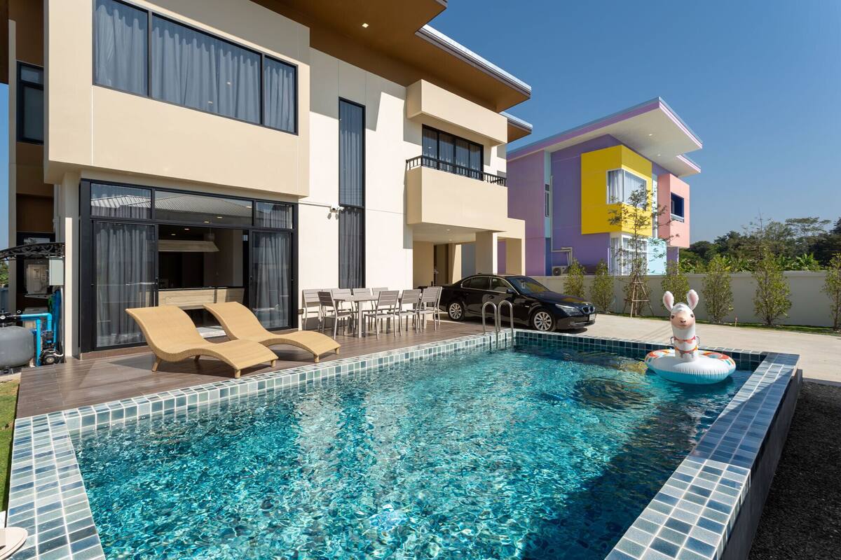 A modern pool area with lounge chairs, a car, and a building with balconies.