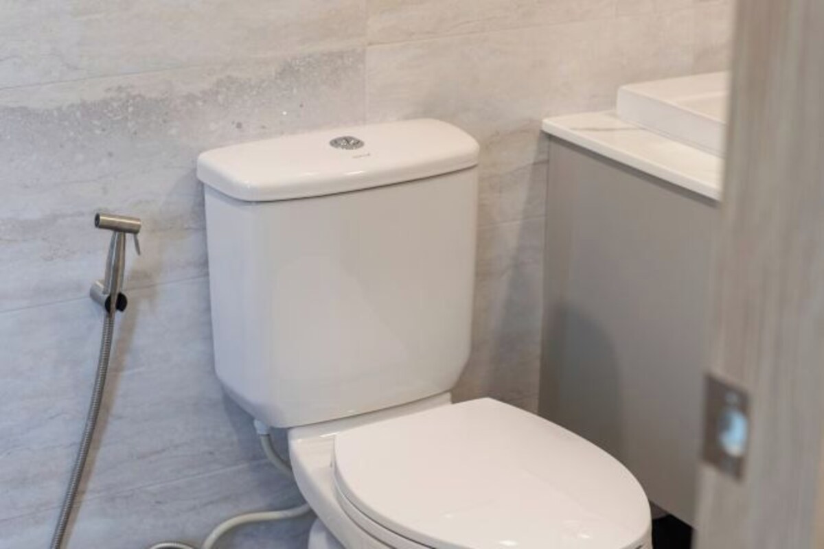 A modern bathroom with a white toilet, a visible water pipe, and a tiled wall.