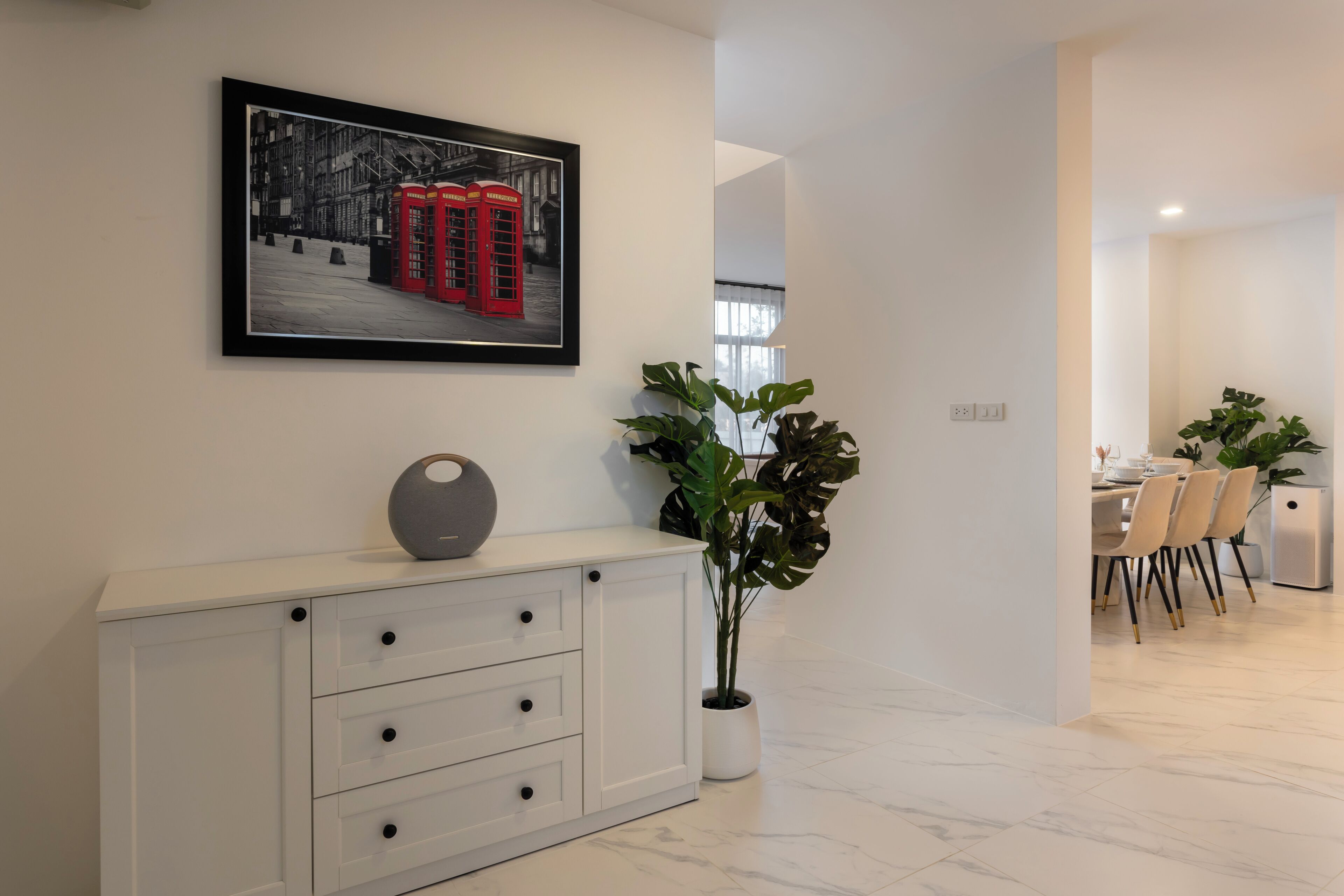 A modern interior with a white console table, a framed picture of red telephone booths, and a potted plant.