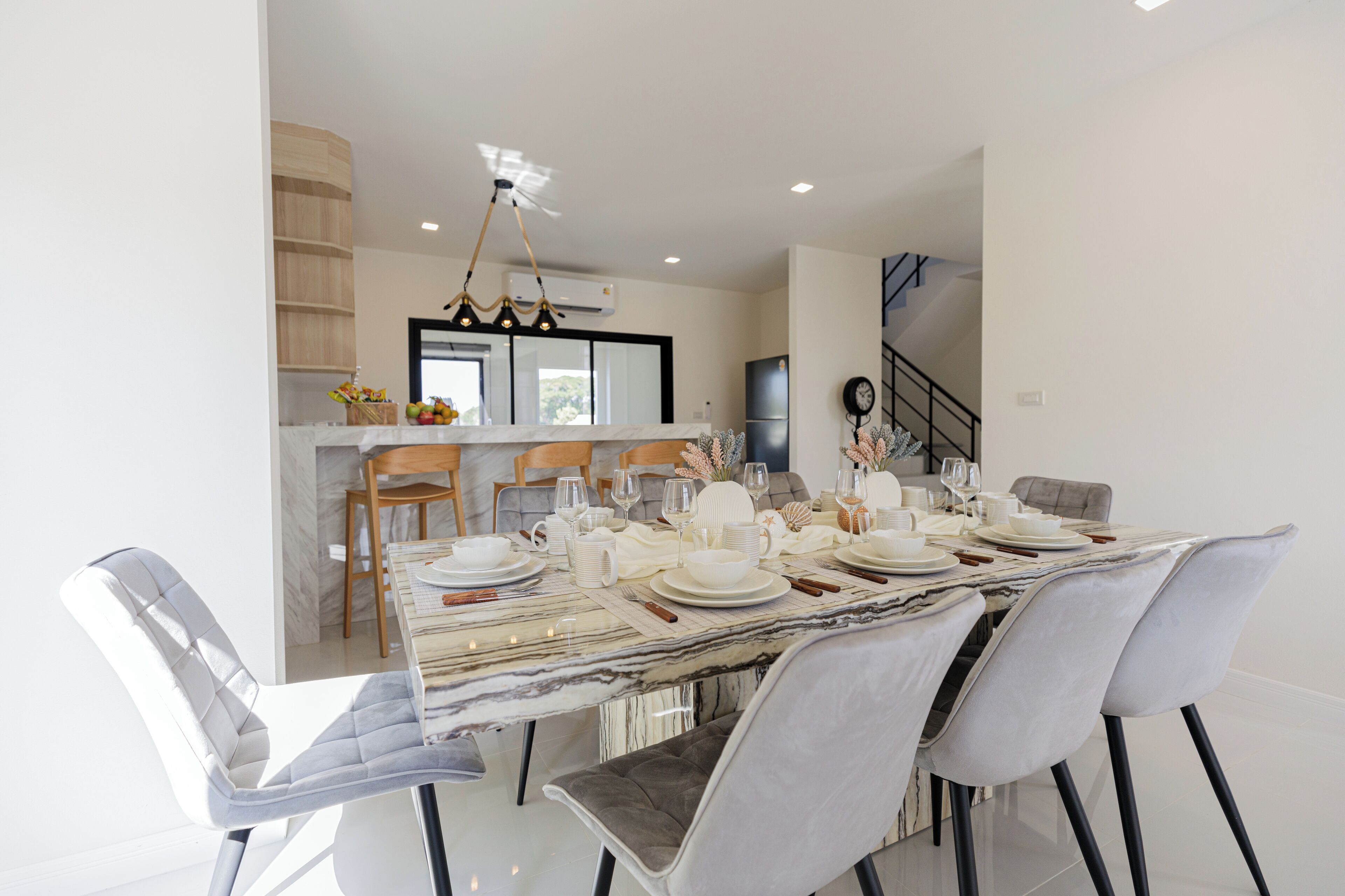 Un espace de salle à manger moderne avec une table en marbre, des chaises blanches et un lustre.