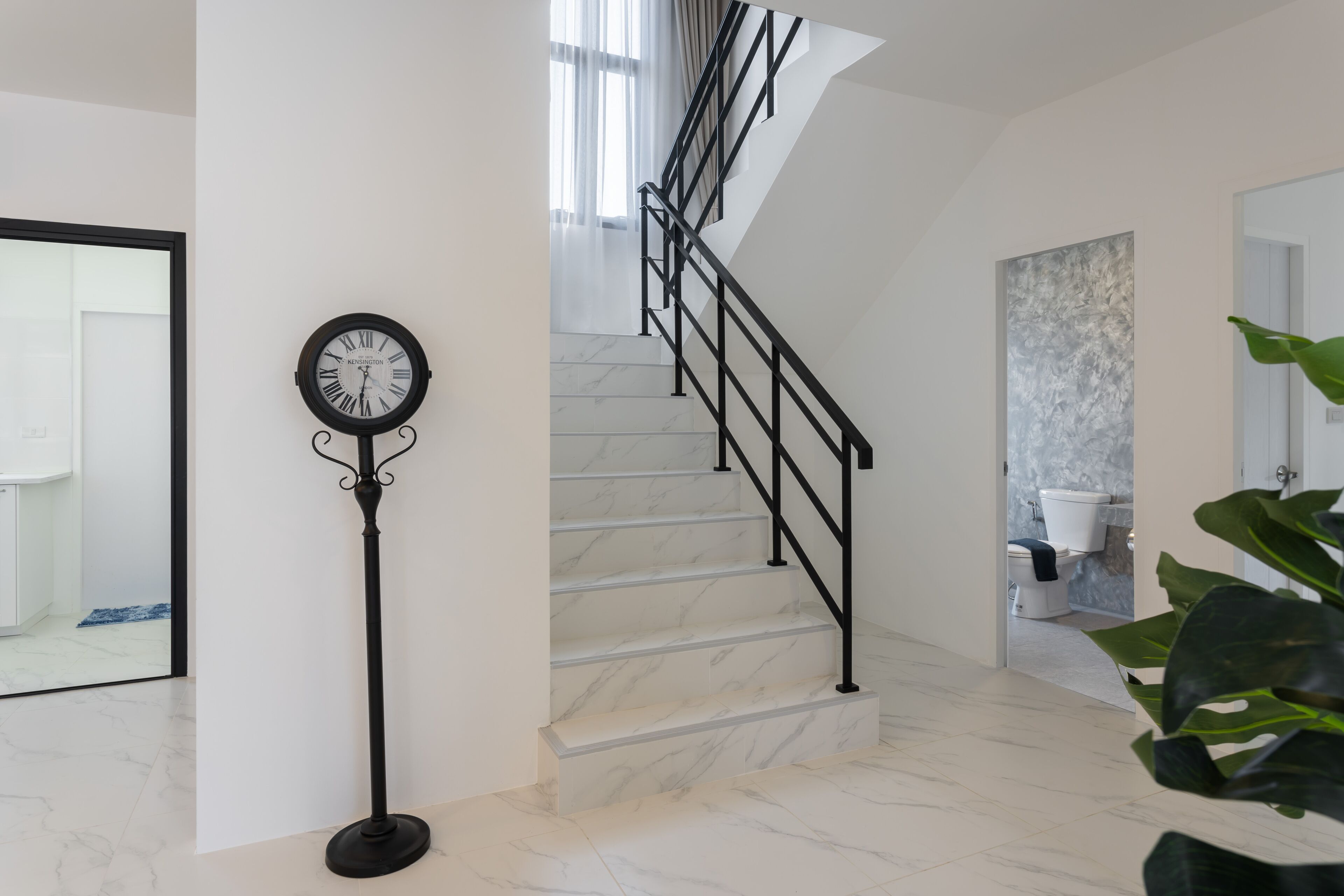 Una escalera con barandillas negras, un reloj y una planta en maceta.