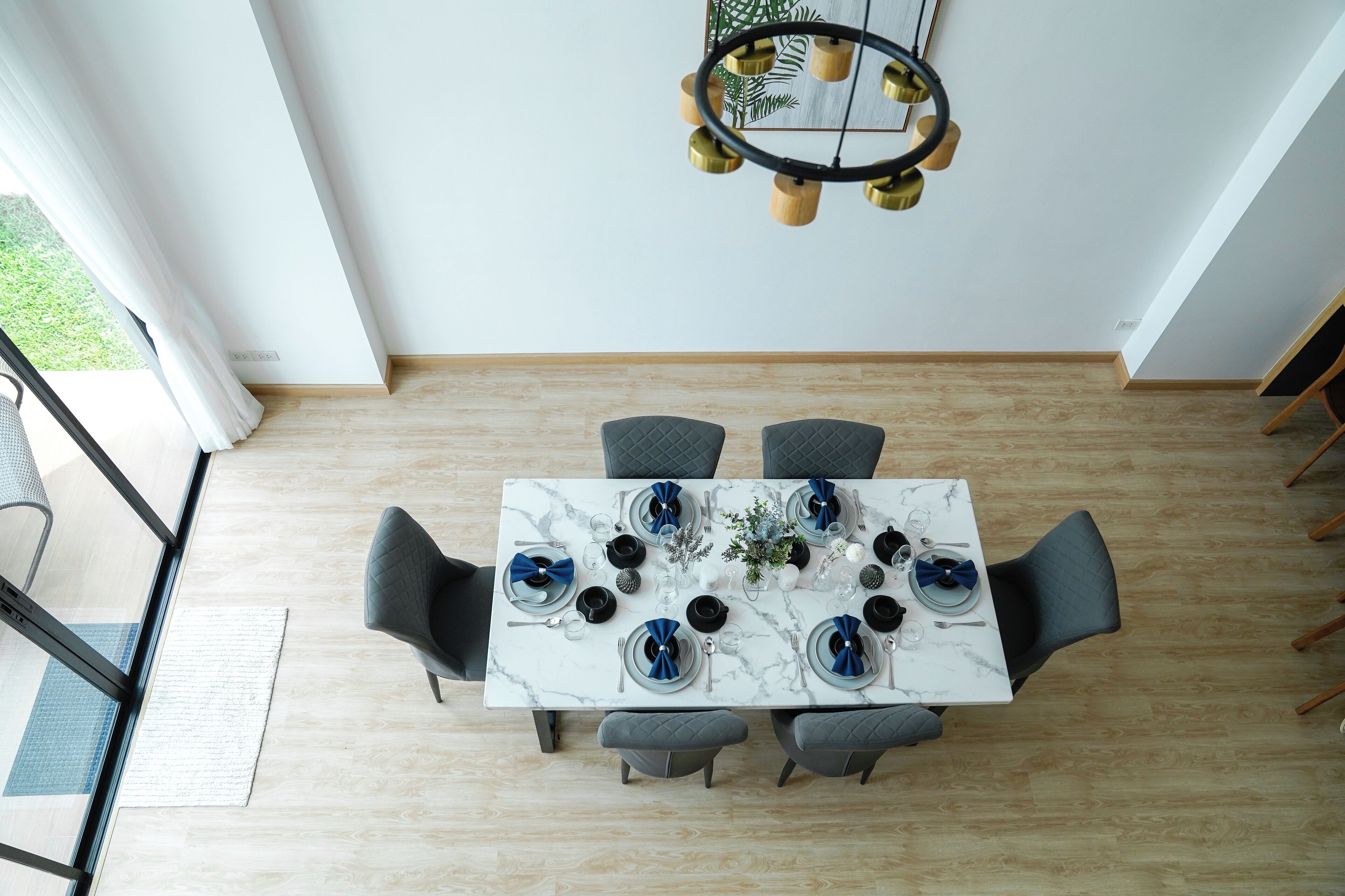 A dining area with a marble table, grey chairs, and a hanging light fixture.