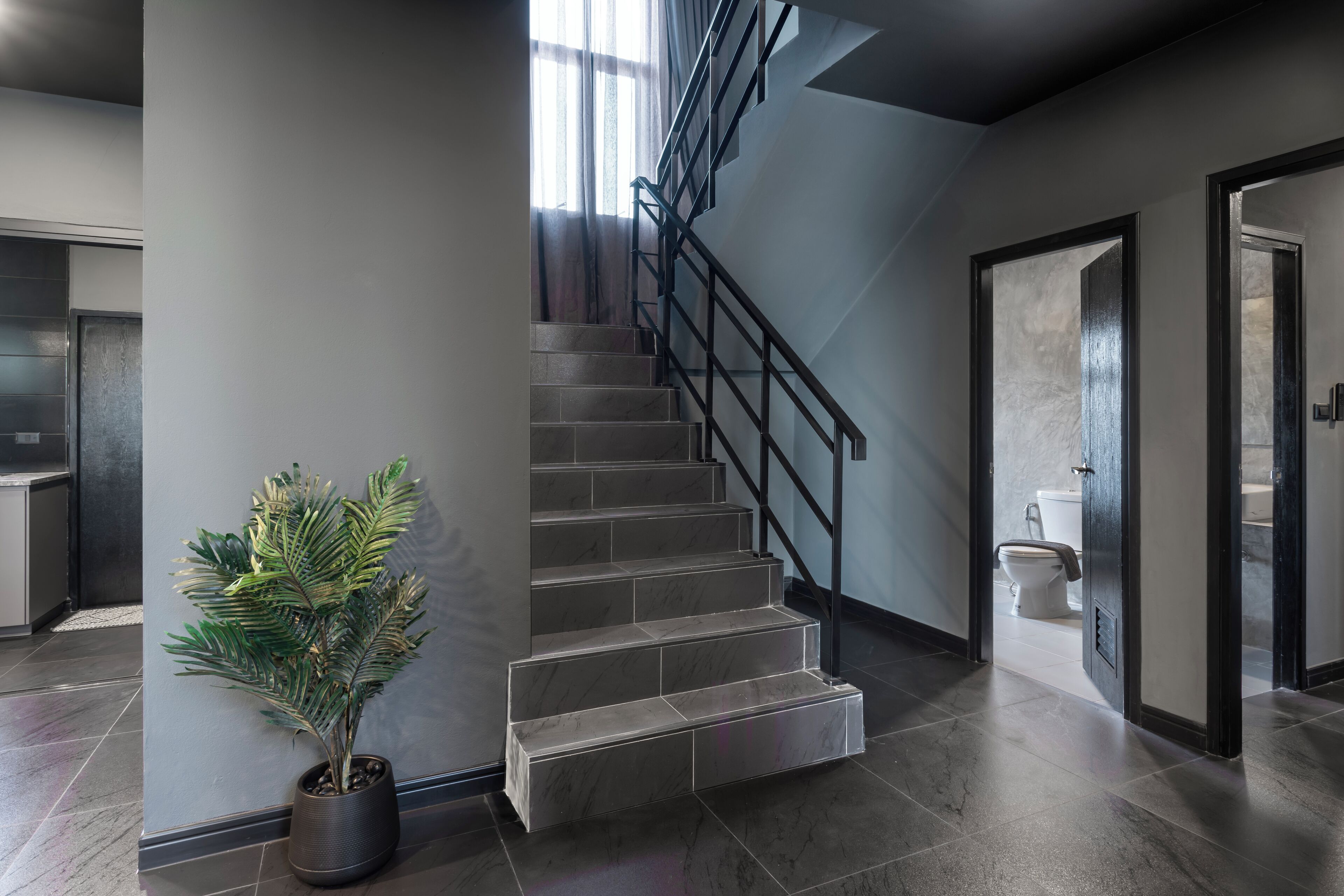 A modern staircase with a metal railing, a potted plant, and a view of a bathroom.