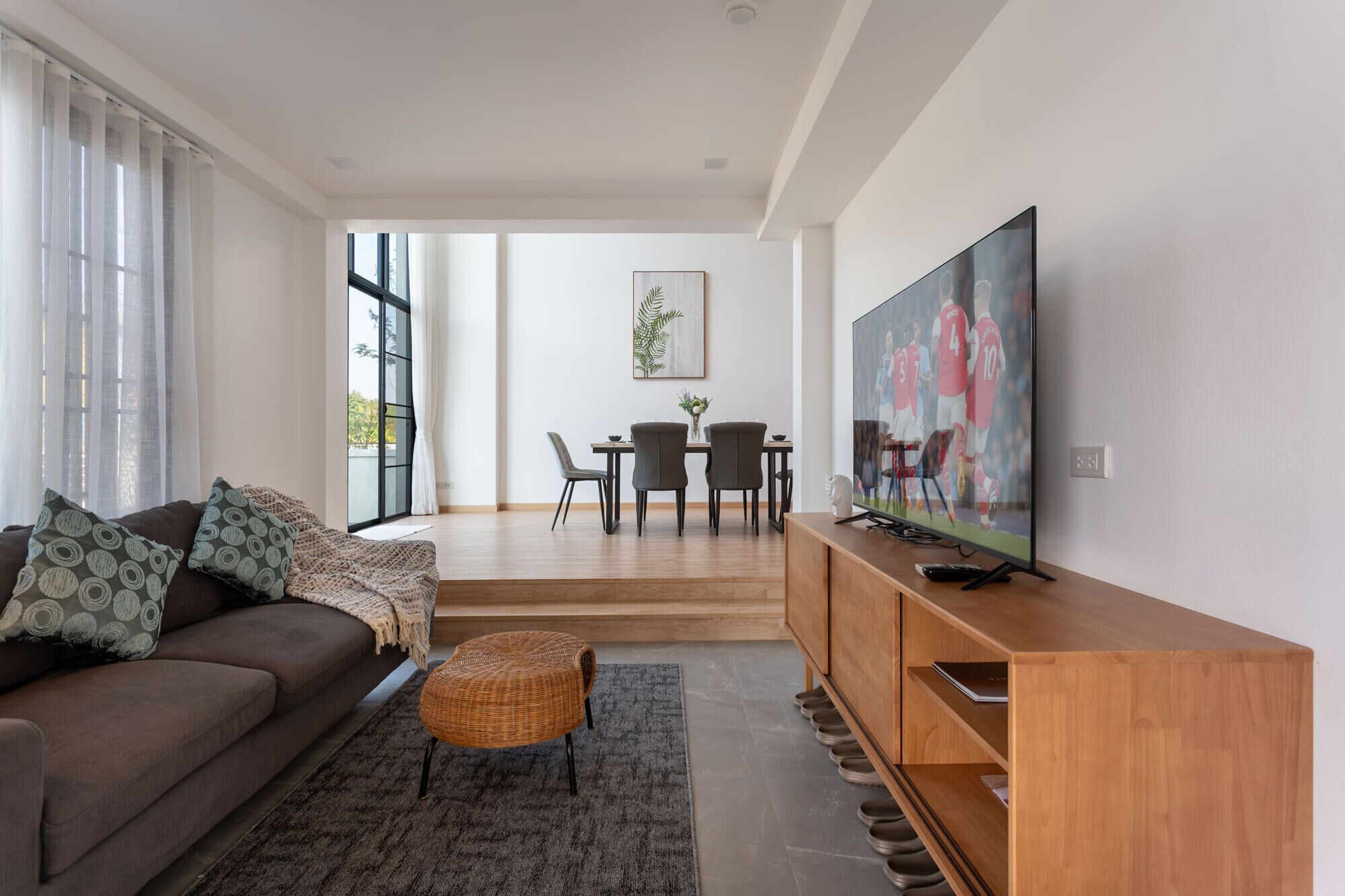 A modern living room with a sofa, a television, and a dining area with chairs and a table.