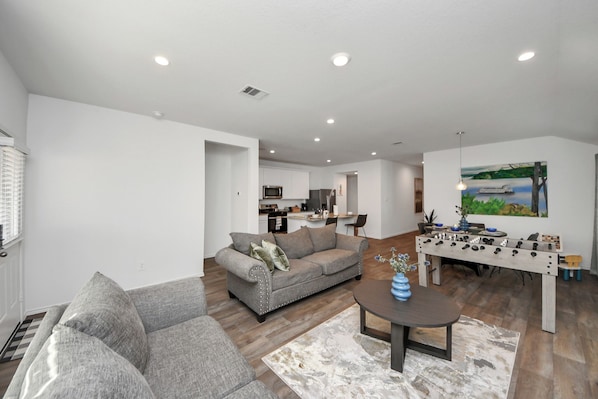 A modern living room with a gray sofa, a coffee table, and a foosball table. - Brand New Construction Escape in Katy-Fulshear with community pool access. (Fulshear)
