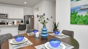 Een moderne eethoek met een ronde tafel voor vier personen, blauwe glazen en een vaas met bloemen.