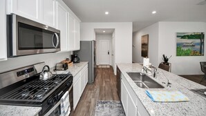 Een moderne keuken met witte kasten, roestvrijstalen apparatuur, een granieten aanrechtblad en uitzicht op de eetruimte.