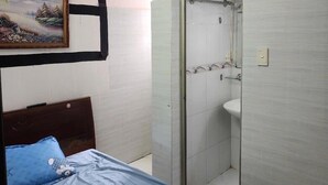 Un dormitorio con cama, un cuadro, un baño con ducha y una puerta con ganchos.