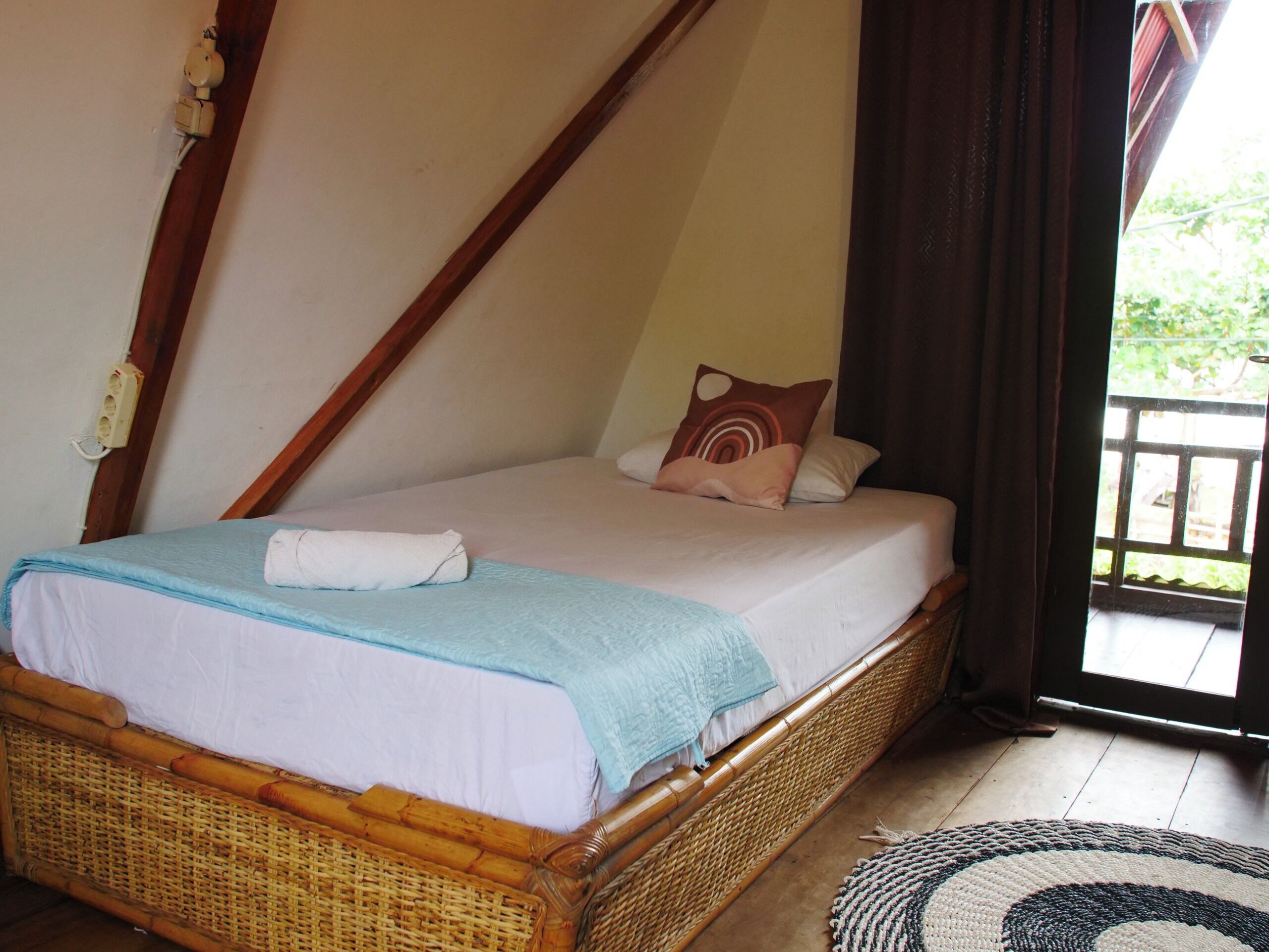 A single bed with a blue blanket and white sheets, a wooden headboard, and a wicker footboard.