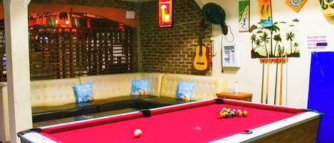 A pool table in a room with a brick wall, a guitar, and a billiard cue rack.