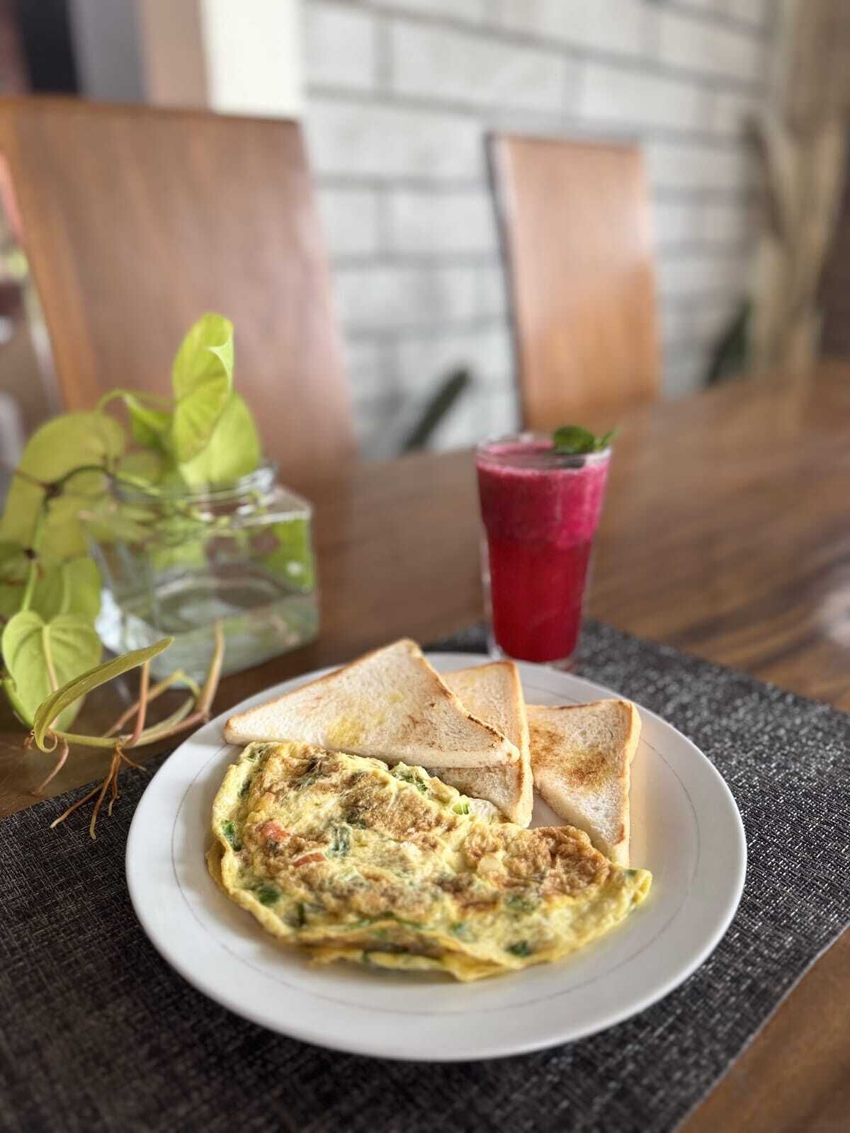 Un plat amb una torrada, una truita, una beguda vermella i una planta verda sobre una taula.
