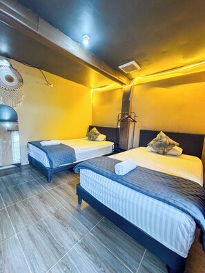 A hotel room with two beds, a hanging light fixture, and a wall-mounted heater.