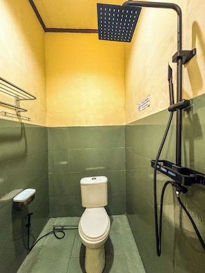 A small, compact bathroom with a toilet, a showerhead, and a hand dryer.