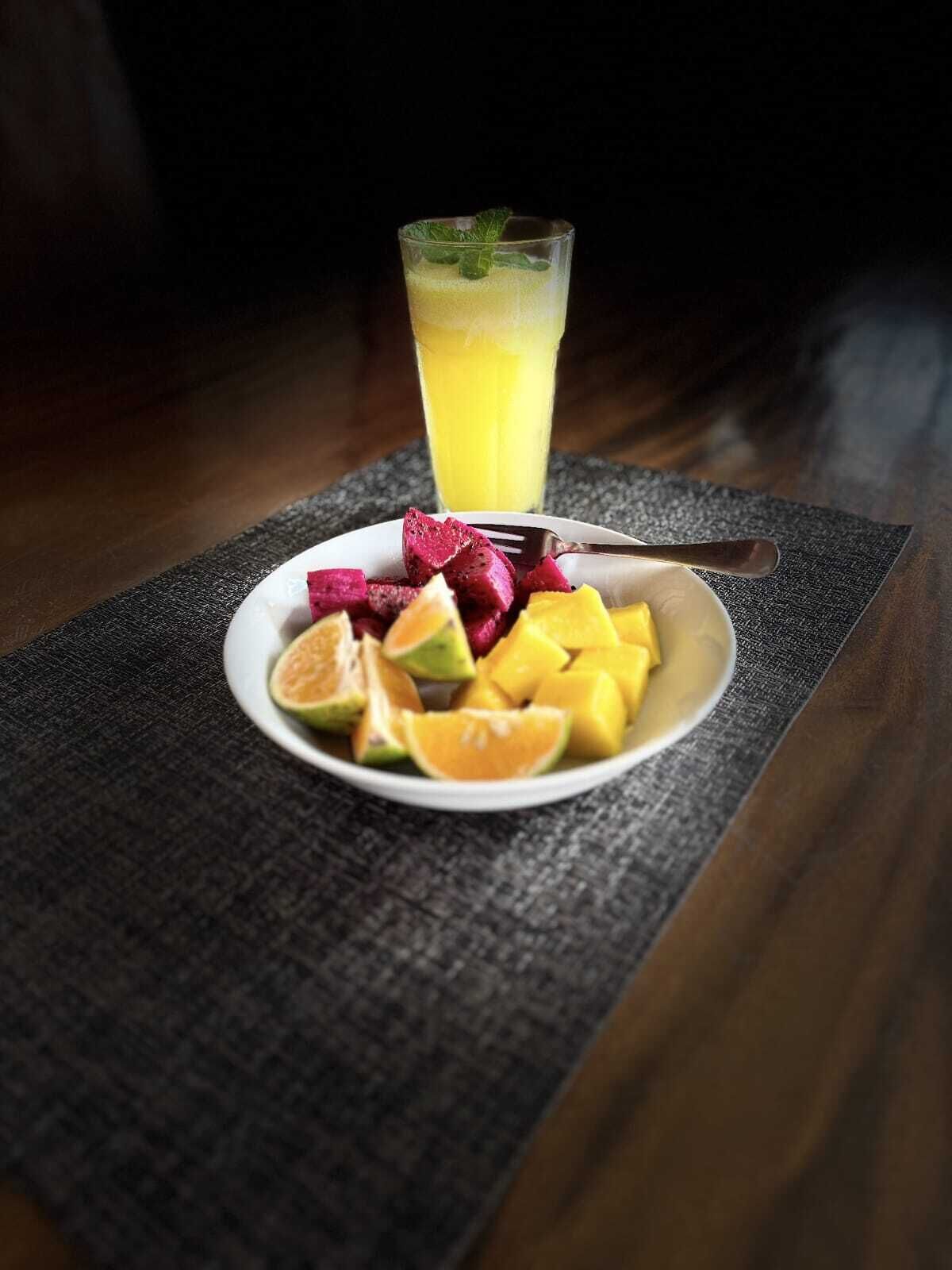 A plate of fruit and a glass of juice on a textured tablecloth.