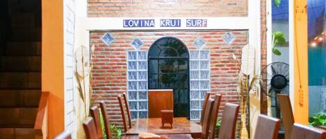 Un comedor con pared de ladrillo, un letrero que dice "LOVINA KRUII SURF" y una larga mesa de madera con sillas.