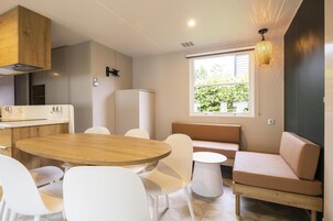 Una cocina moderna con una mesa de madera y sillas blancas, horno empotrado y ventana con vistas a zonas verdes.