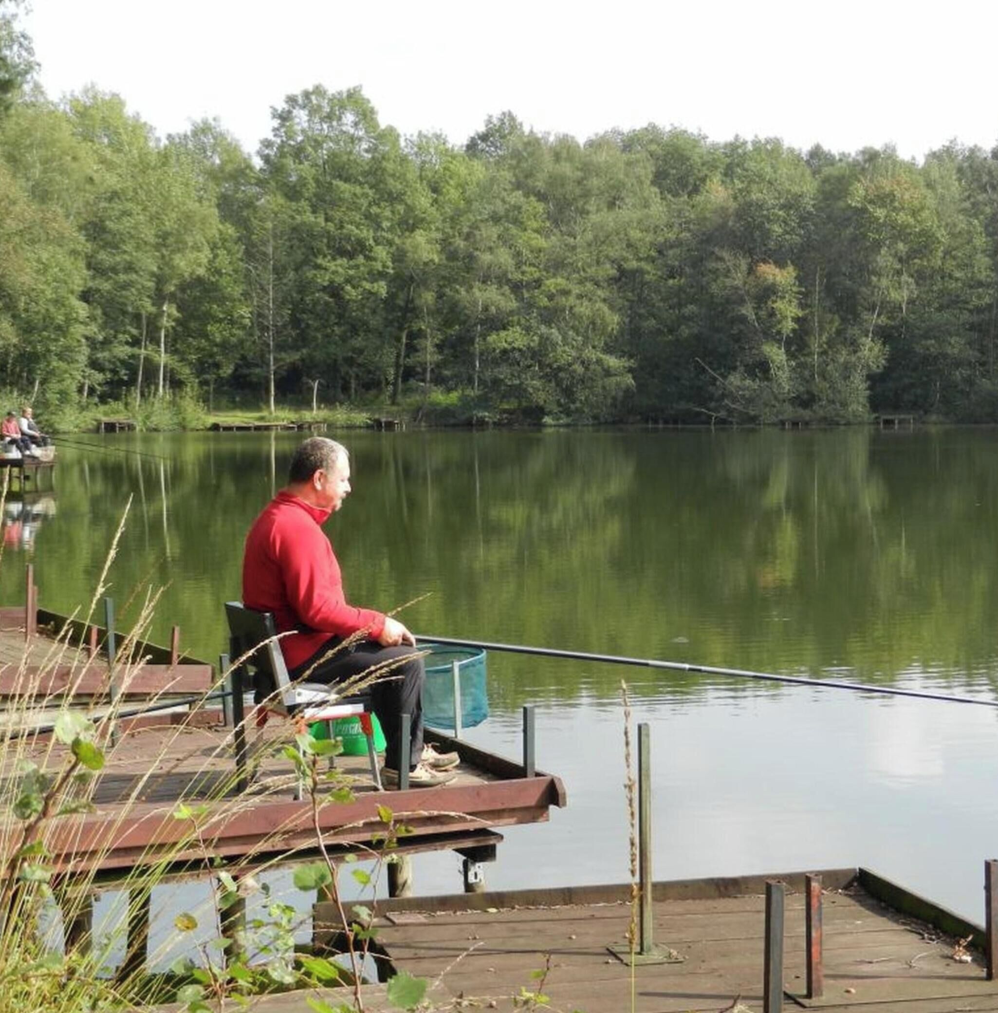 A man sitting on a dock by a calm lake with trees in the background.