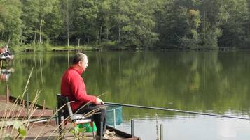 A man sitting on a dock by a calm lake with trees in the background.