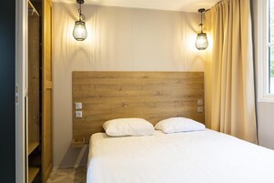 Un dormitorio con cabecera de madera, dos lámparas de noche, una cama con ropa blanca y una ventana con cortinas.