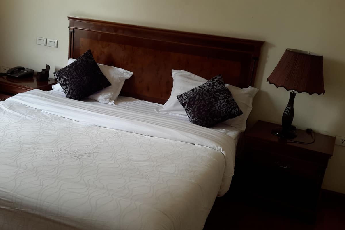 Una cama bien hecha con sábanas blancas y almohadas estampadas, un cabecero de madera, una mesita de noche con una lámpara y un teléfono.