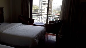 Habitación de hotel con cama, una silla, una mesita y vista a la ciudad a través de una ventana.