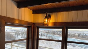 A corner of a room with three windows overlooking a snowy landscape, a wooden bench, and a wall-mounted lantern. - Classy Hillside Tiny House (Monarch)