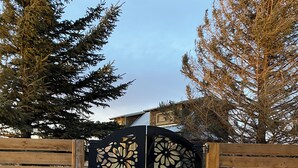 A black gate with intricate cut-out designs, flanked by wooden fences and a concrete pathway leading to a building. - Classy Hillside Tiny House (Monarch)