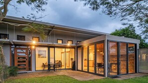 A modern house with a glass-enclosed patio, a dining area, and a kitchen visible through the glass.