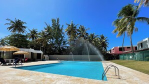 Ein Schwimmbecken mit einer Fontäne, Liegestühlen und Palmen im Hintergrund.