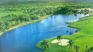 Ein Golfplatz mit Teich, Palmen und Bergen im Hintergrund.