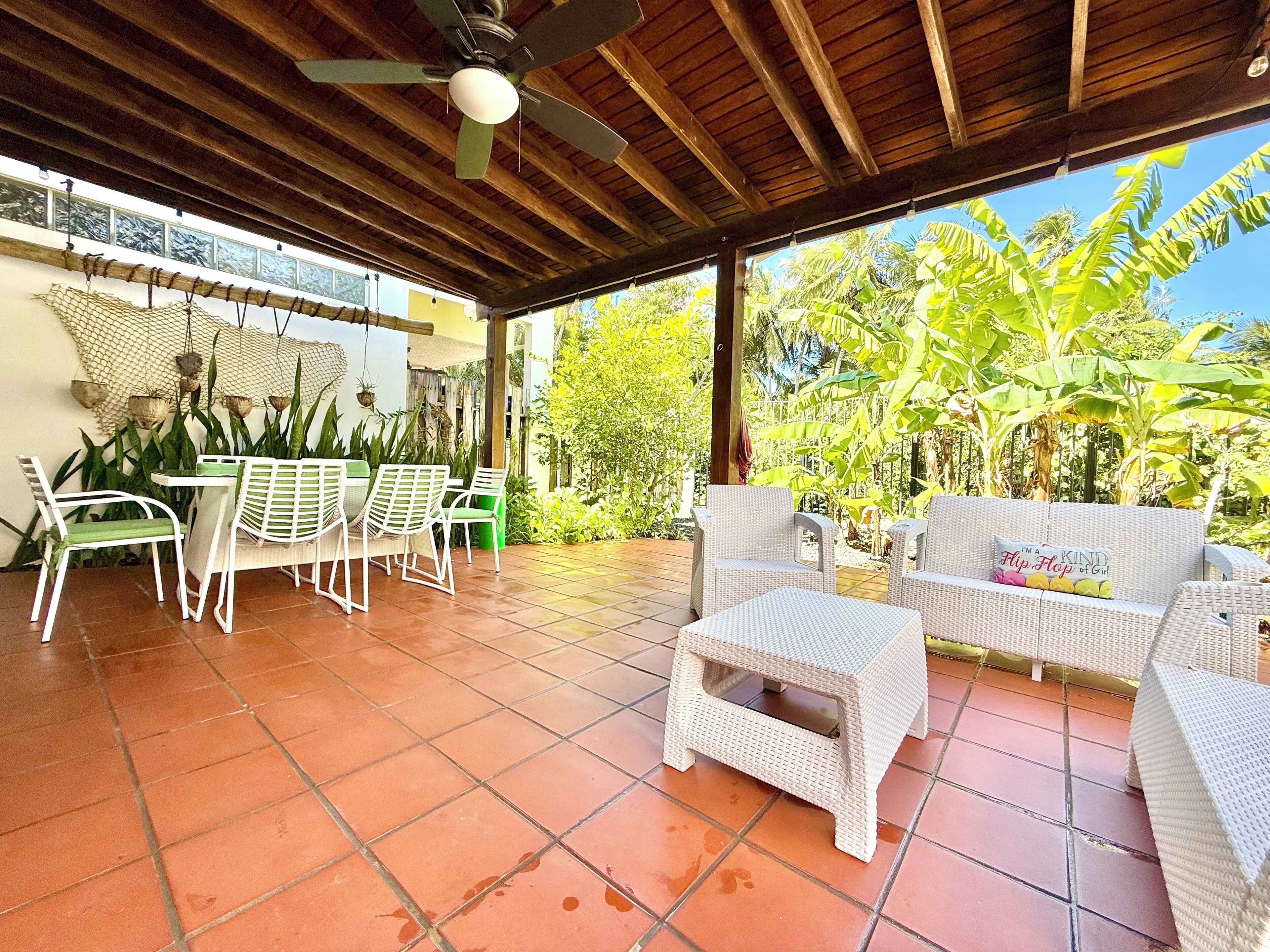 Eine Terrasse im Freien mit Fliesenboden, Korbmöbeln und Deckenventilator.