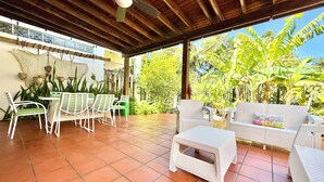 Eine überdachte Terrasse mit Korbmöbeln, einem Deckenventilator und Blick auf üppiges Grün.