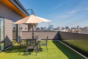 Une terrasse sur le toit, avec une table et des chaises, un parasol beige et une vue sur les toits de la ville.